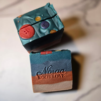 Noraa Body Love Sweata Weatha Bar Soap with fall-inspired tones, topped with playful soap buttons and layered colors that evoke a cozy, seasonal feel.