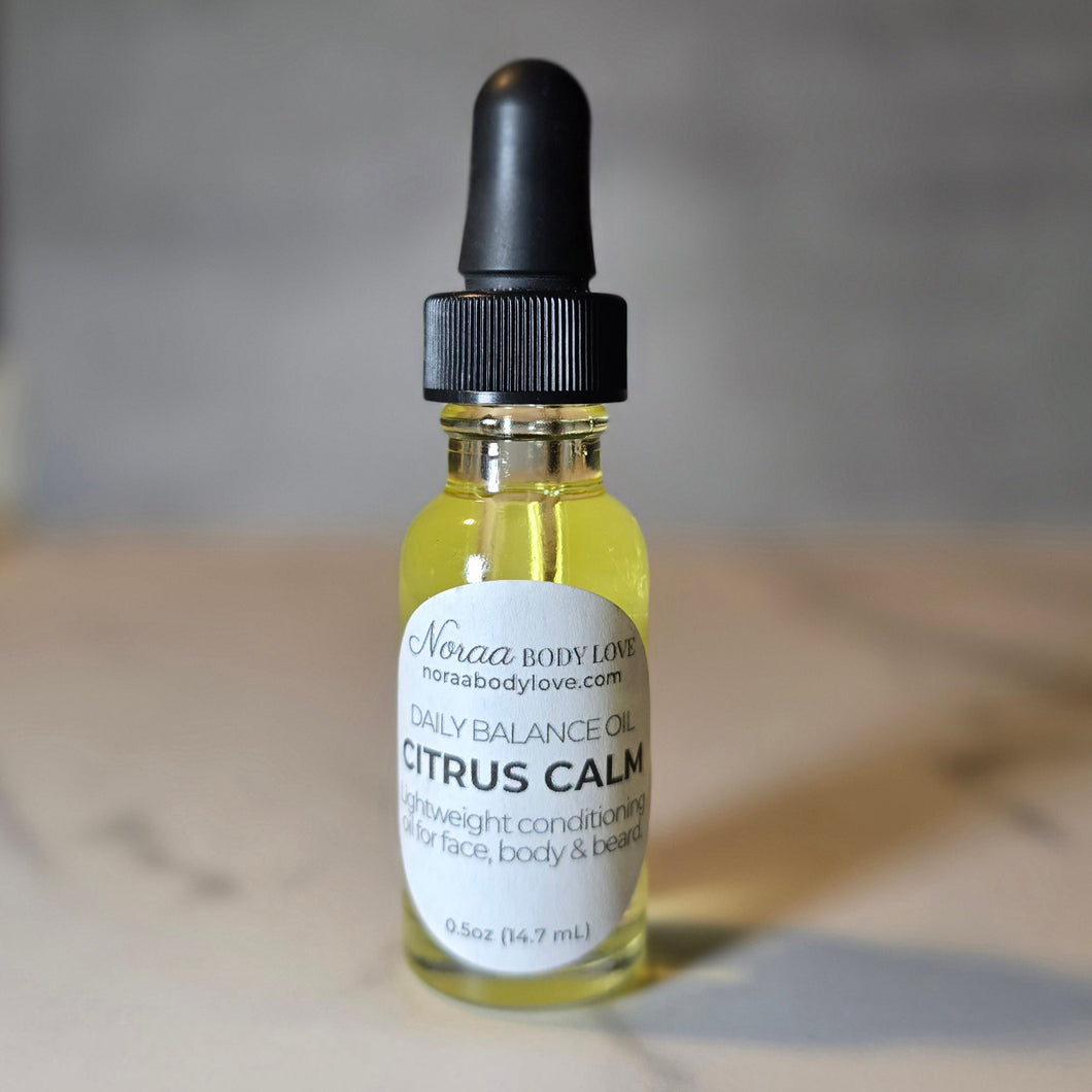 Noraa Body Love Citrus Calm Daily Balance Oil in a clear dropper bottle with a black cap and minimalist label, shown on a marble surface with soft lighting.
